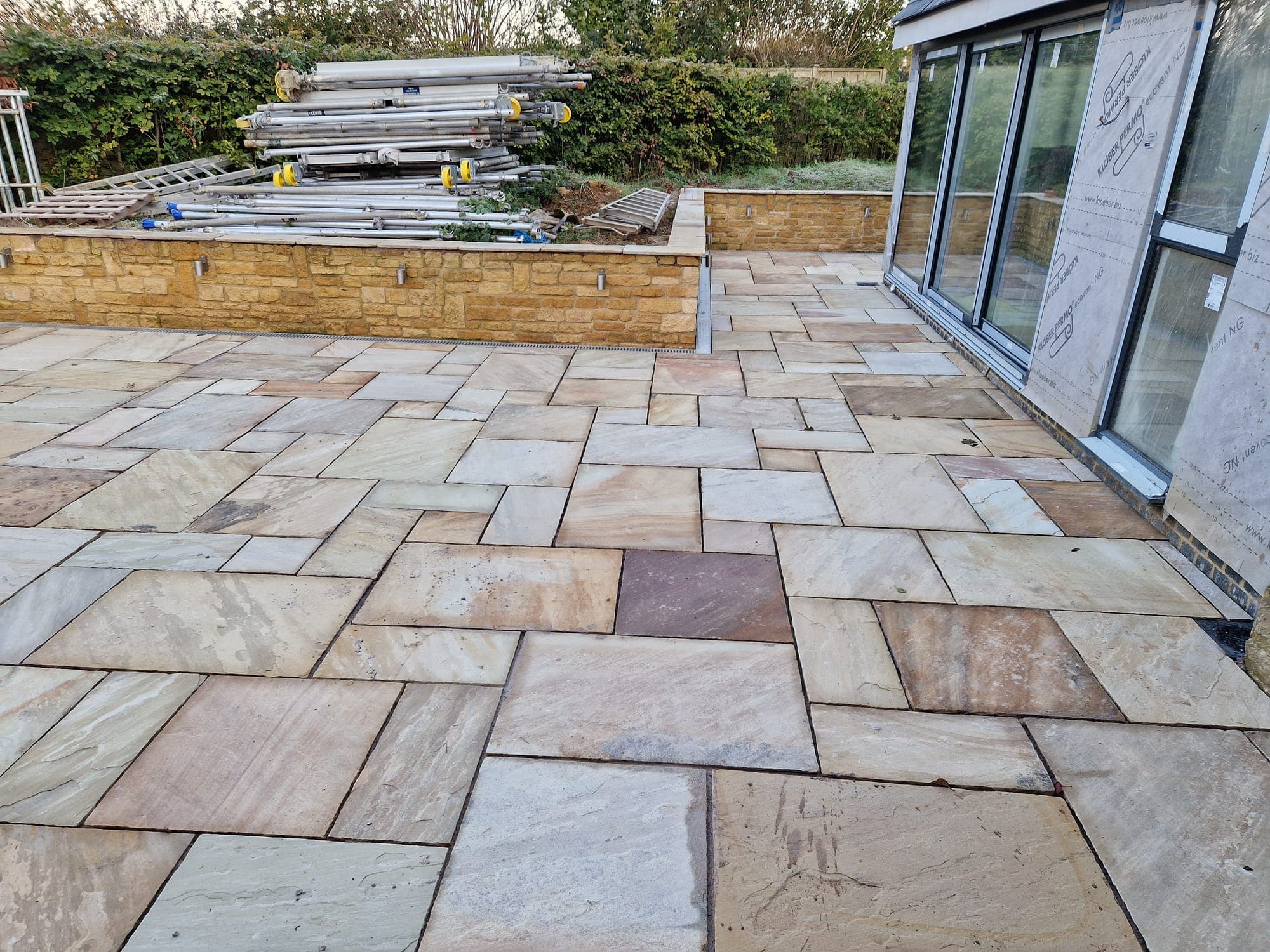 Terrace paving being laid, materials stacked by the extension